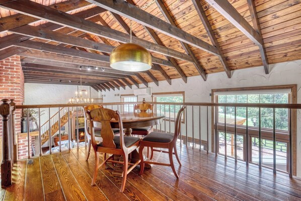 Una habitación amplia con techo alto, vigas de madera, una mesa de comedor con sillas y ventanas grandes.