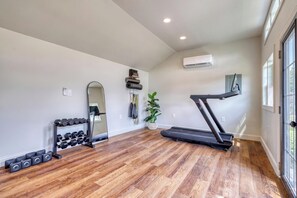 A spacious room with a wooden floor, a treadmill, a mirror, and a wall-mounted air conditioning unit. - Carriage House King Suite near Battlefield - Patio, Hot Tub, Sauna (Gettysburg)