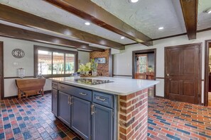 A kitchen with a central island, blue cabinets, a brick accent wall, and a large window. - Carriage House King Suite near Battlefield - Patio, Hot Tub, Sauna (Gettysburg)