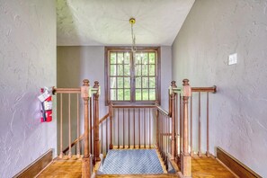 Una escalera con balaustres de madera y barandilla, que conduce a un rellano con vistas a árboles a través de una ventana.