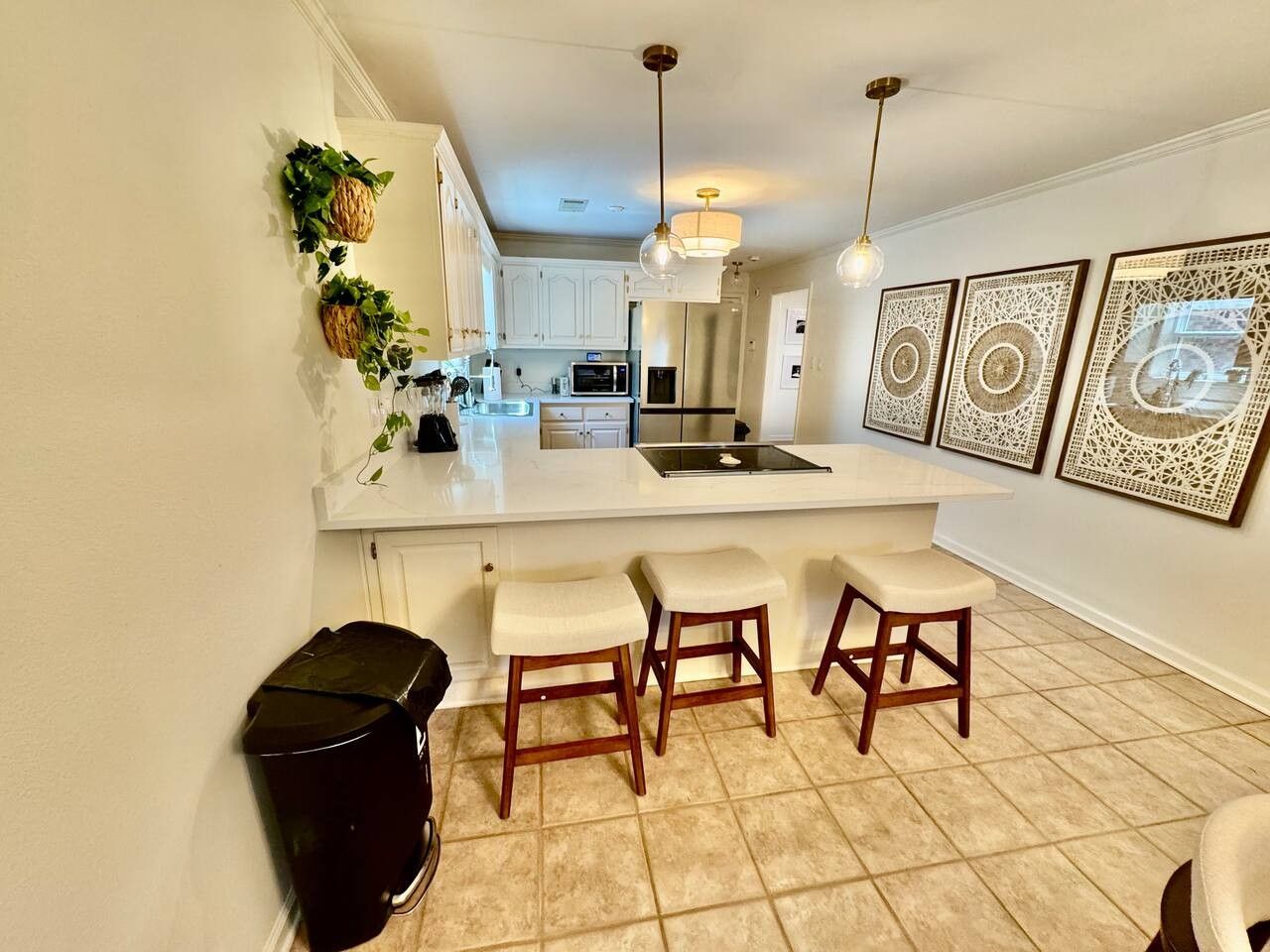 A kitchen with a white countertop, wooden stools, and a trash bin.