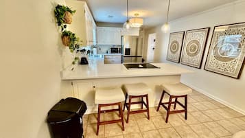 A kitchen with a white countertop, wooden stools, and a trash bin.