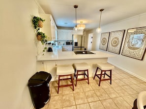 A kitchen with a white countertop, wooden stools, and a trash bin.