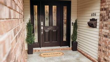 A dark wooden front door with diamond patterns, a welcome mat, and two potted plants on either side.