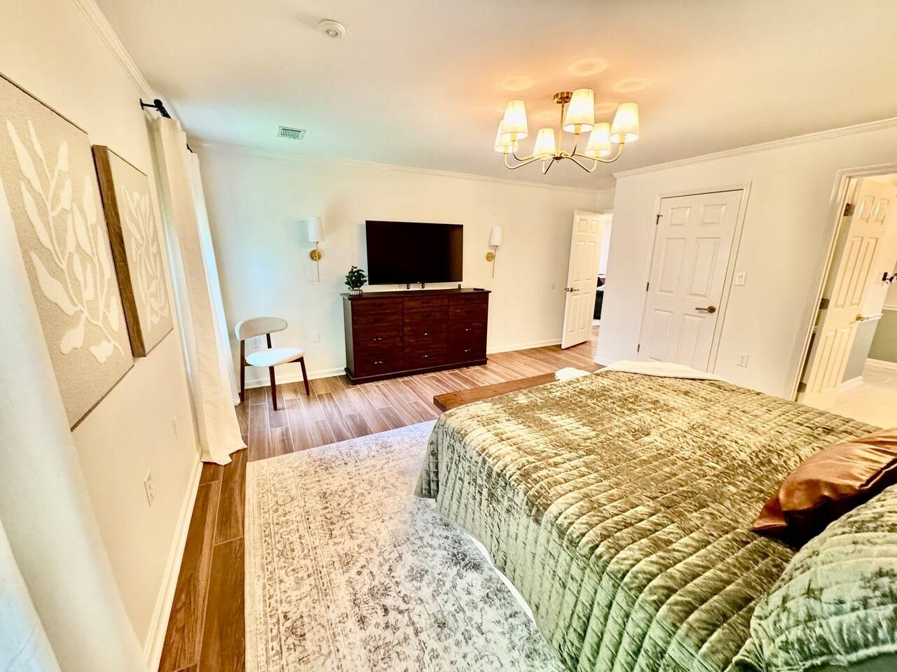A bedroom with a bed, a dresser, a television, and a chandelier.