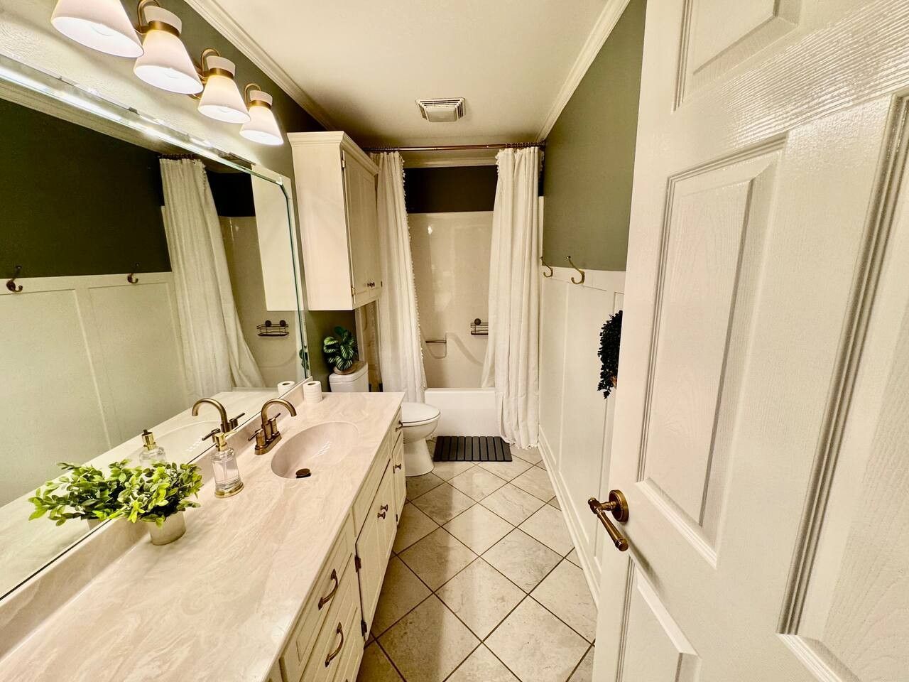 Une salle de bain avec un double lavabo, des toilettes, une douche avec rideau et un miroir avec éclairage intégré.