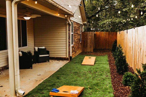 Un jardin avec une terrasse en bois, un patio couvert et une petite pelouse agrémentée de deux jardinières en bois.