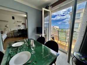 Een eethoek met een gedekte tafel voor twee, een televisie en een balkon met uitzicht op zee.