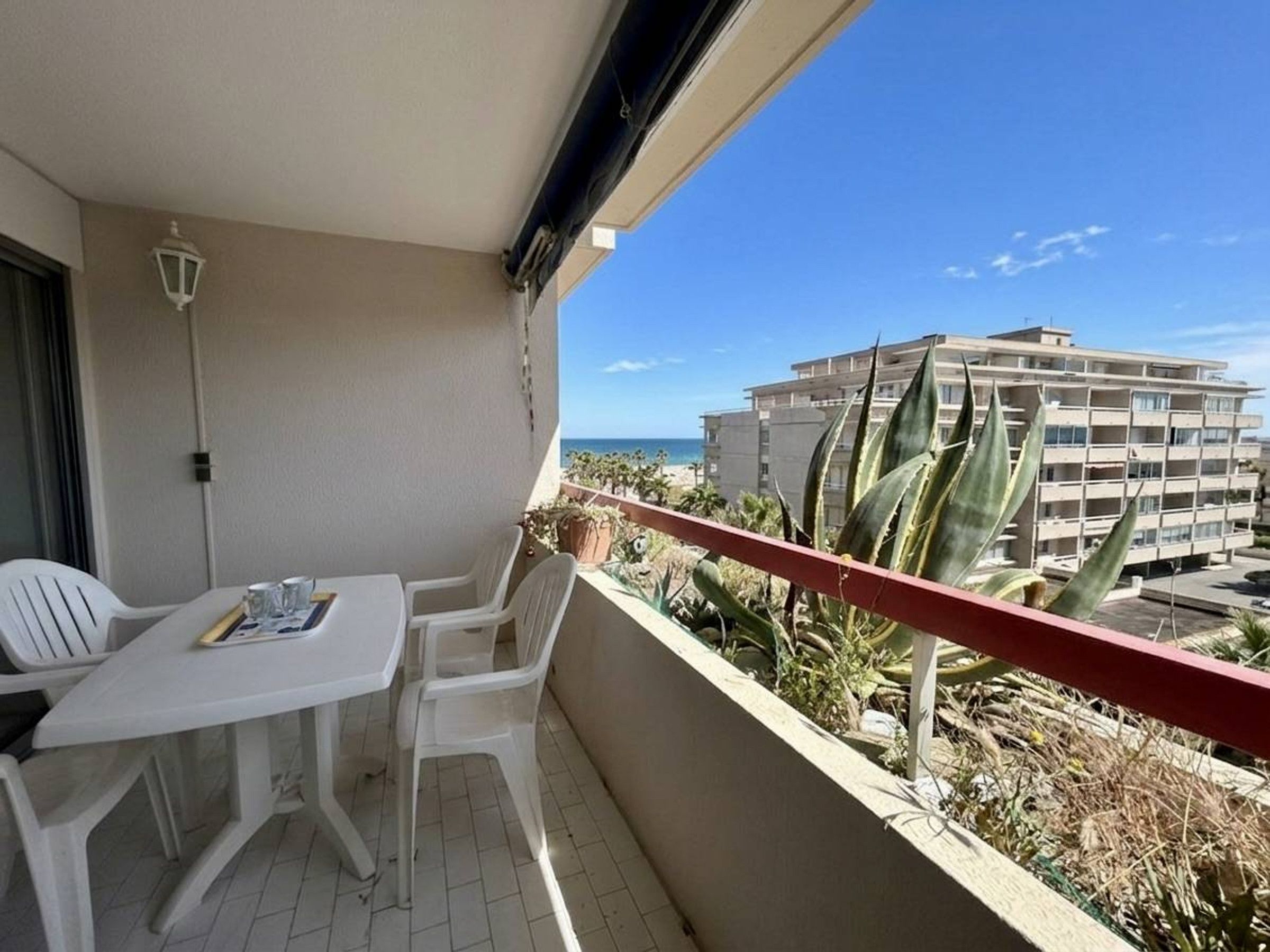 A balcony with a table and chairs, overlooking a building and the sea.
