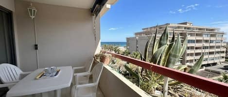 A balcony with a table and chairs, overlooking a building and the sea.