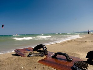 A beach scene with a surfboard and a helmet on the sand, a clear sky, and waves in the background. - T3 apartment, parking, sea view - 6 guests (Canet-en-Roussillon)
