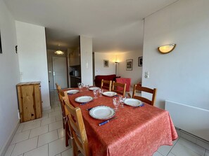 A dining area with a table set for four, wooden chairs, a red tablecloth, and a wall-mounted light fixture. - T3 apartment, parking, sea view - 6 guests (Canet-en-Roussillon)