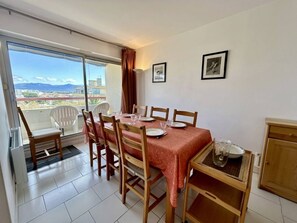 A dining area with a table set for four, chairs, a view through a glass door, and a small cabinet. - T3 apartment, parking, sea view - 6 guests (Canet-en-Roussillon)