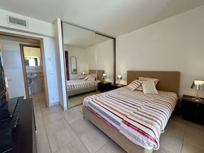 Ein Hotelzimmer mit einem Bett, Nachttischen, einem Spiegel, einem Schreibtisch und einem Kleiderschrank.