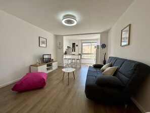 Ein kompakter Wohnbereich mit einem dunklen Sofa, einem kleinen Esstisch und einem rosafarbenen Kissen.