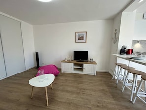 Ein kompakter Wohnraum mit Fernseher, einer kleinen Essecke und einer Küchenzeile.