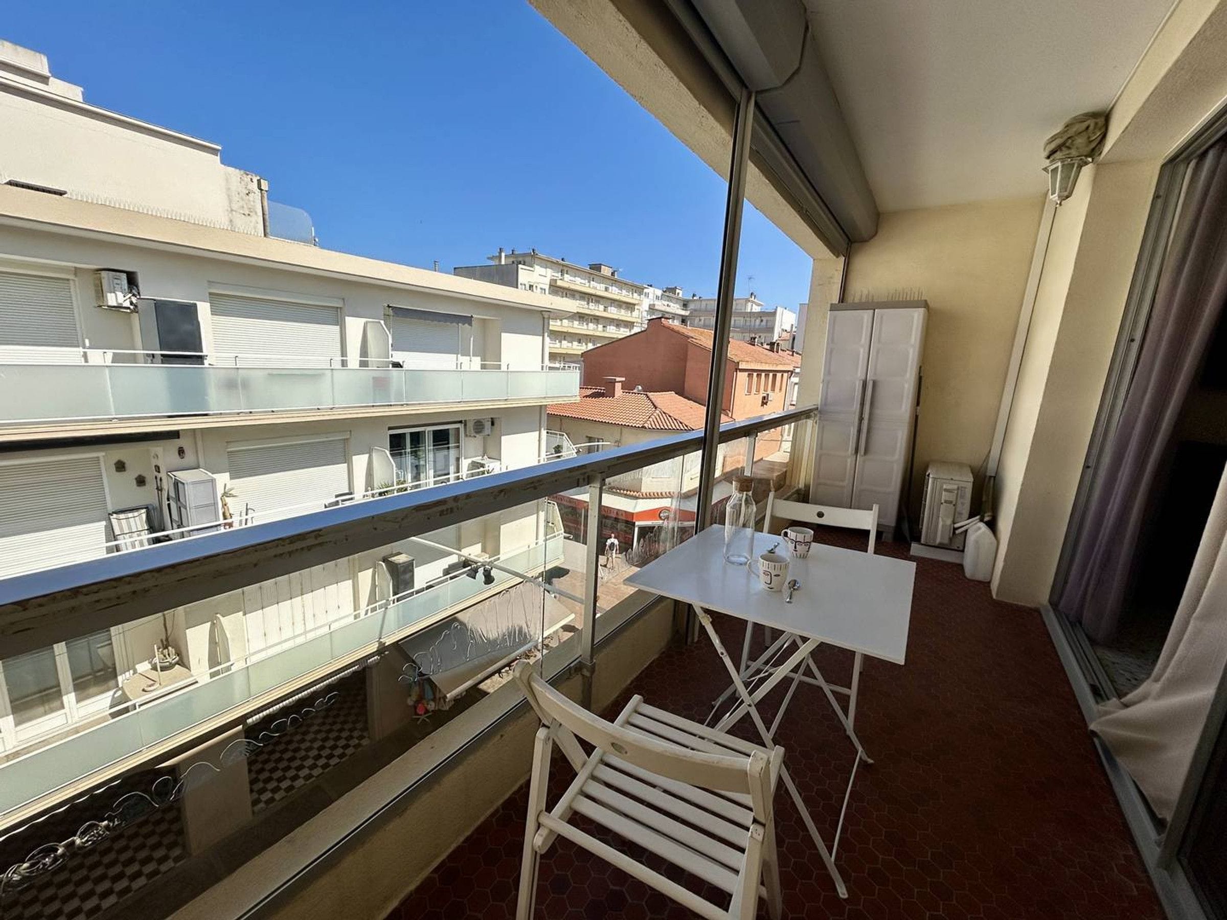 A balcony with a table and chairs, a view of the cityscape, and a window with curtains.