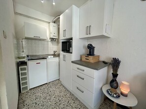 A compact kitchen with white cabinets, a microwave, and a coffee machine. - Studio with AC near beach - 4 guests (Canet-en-Roussillon)