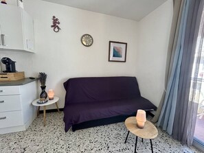 A compact living space with a sofa, a small round table with a candle, a clock, and a framed picture on the wall. - Studio with AC near beach - 4 guests (Canet-en-Roussillon)