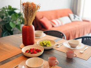 Ein Esstisch mit einer Vase getrockneter Blumen, Schalen mit Erdbeeren und Trauben sowie zwei rosa Tassen.
