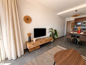 Ein modernes Wohnzimmer mit Flachbildfernseher, Holzkonsole, Essbereich und Küche.