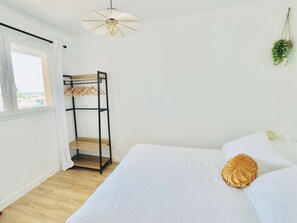 Un dormitorio con una cama individual doble, una planta colgante, una cama con ropa de cama blanca y un ventilador de techo.