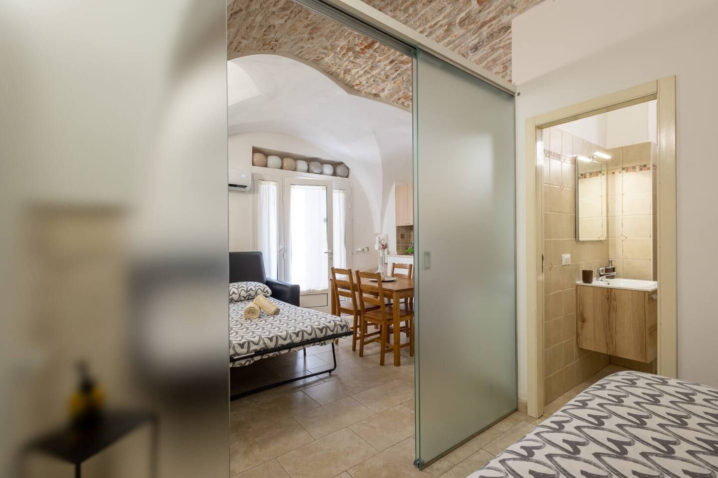 Une chambre moderne avec un lit, un bureau et une chaise. On y trouve également une salle de bain avec un lavabo et un miroir.