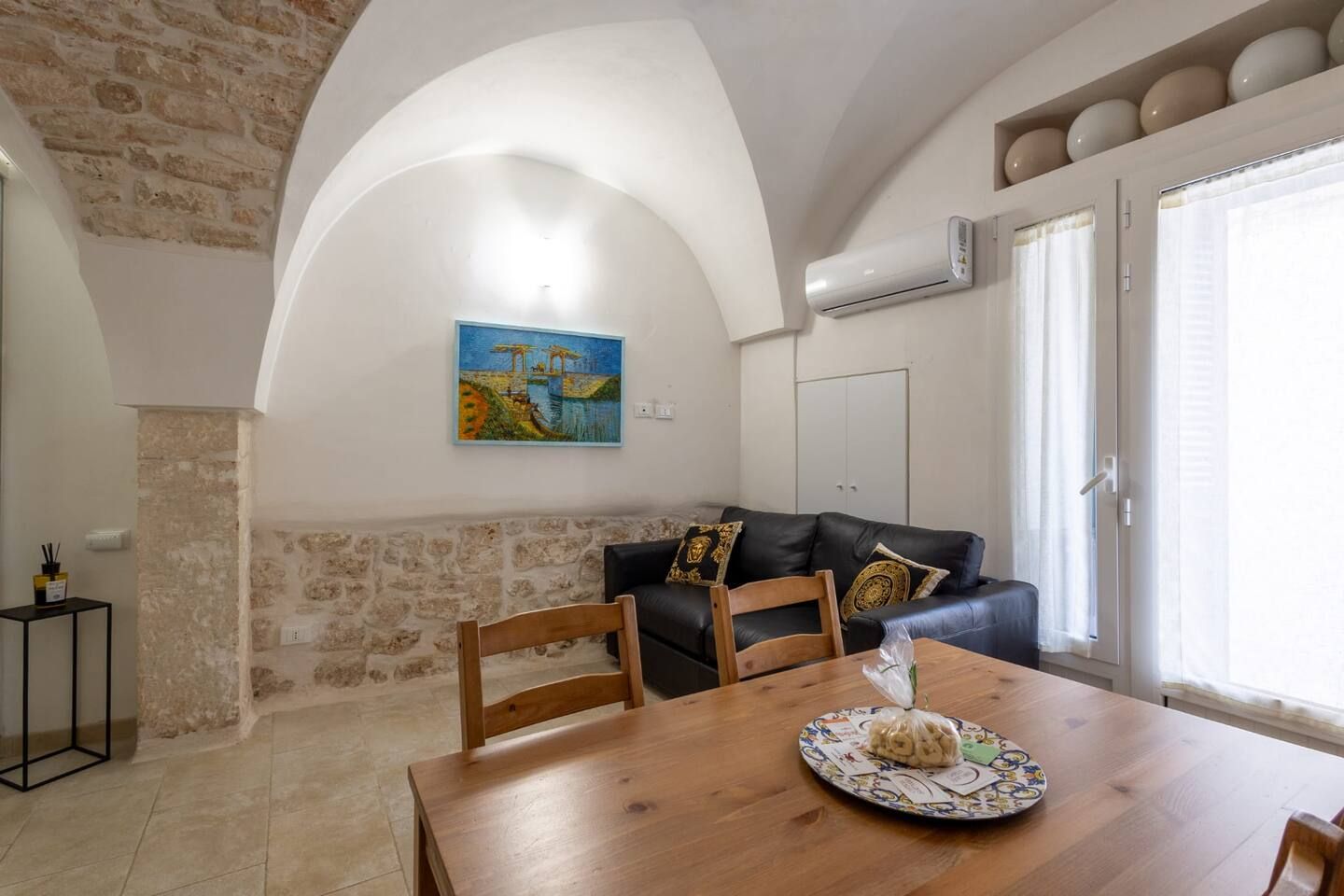 Un coin repas avec une table en bois, des chaises, un tableau accroché au mur et un mur en pierre.
