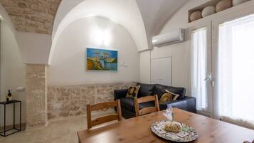 Un coin repas avec une table en bois, des chaises, un tableau accroché au mur et un mur en pierre.