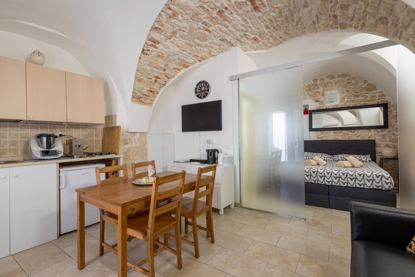 A compact living space with a kitchen, dining area, and a bedroom with a bed and a TV.