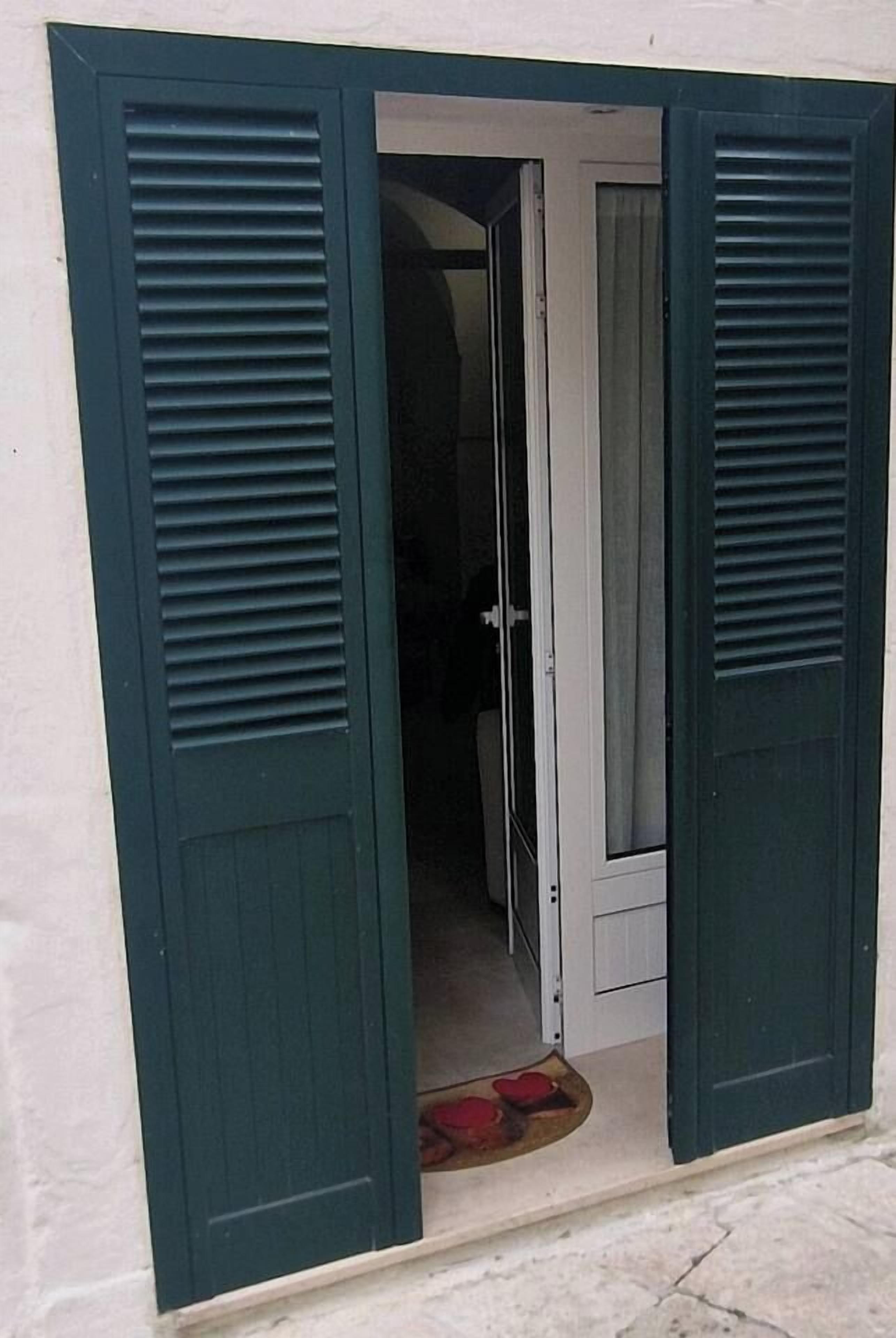 A doorway with a white door and green shutters, leading into a room with a visible doormat.