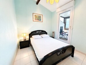 A bedroom with a bed, a nightstand, a lamp, a window, and a door leading to an outdoor area. - Spacious apartment with sea view - 7 guests (Canet-en-Roussillon)