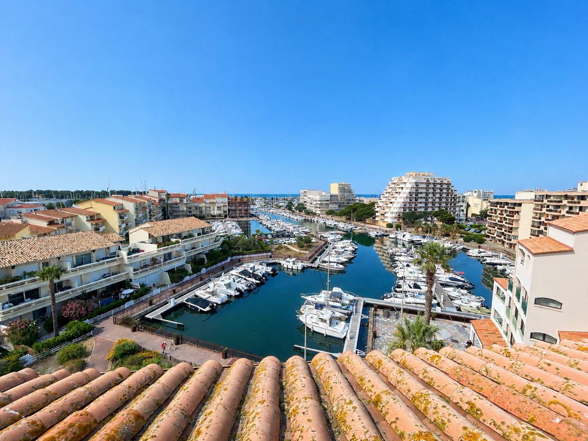 A marina with boats docked, surrounded by residential buildings with terracotta roofs.