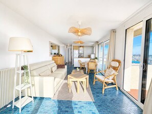 Ein großzügiger Wohnbereich mit Sofa, Esstisch und Stühlen, ein Balkon mit Blick auf den Yachthafen und ein Deckenventilator.