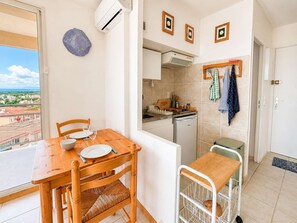 A dining area with a wooden table and chairs, a view through a glass door, a kitchen with a dishwasher, and a small table with a chair. - Studio sea view, AC, pets allowed - 2 guests (Canet-en-Roussillon)