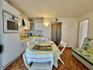 Cozinha compacta com mesa de jantar, cadeiras, micro-ondas e um sofá.