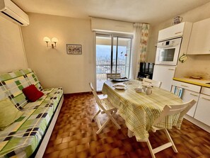Um espaço de estar compacto com sofá, mesa de jantar, cadeiras, uma cozinha compacta e uma varanda com vista.