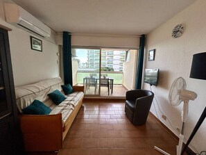 Un saló amb un sofà, una cadira, una televisió i un ventilador.