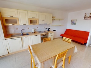 A compact kitchen with a dining table, chairs, a red sofa, and a tiled backsplash. - Spacious studio with AC and terrace - 4 guests (Menton)