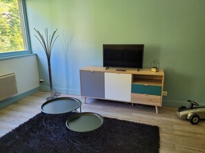 A room with a TV on a wooden cabinet, a small table with a black rug, and a toy car. - Spacious apartment near slopes - 8 guests (Flaine)