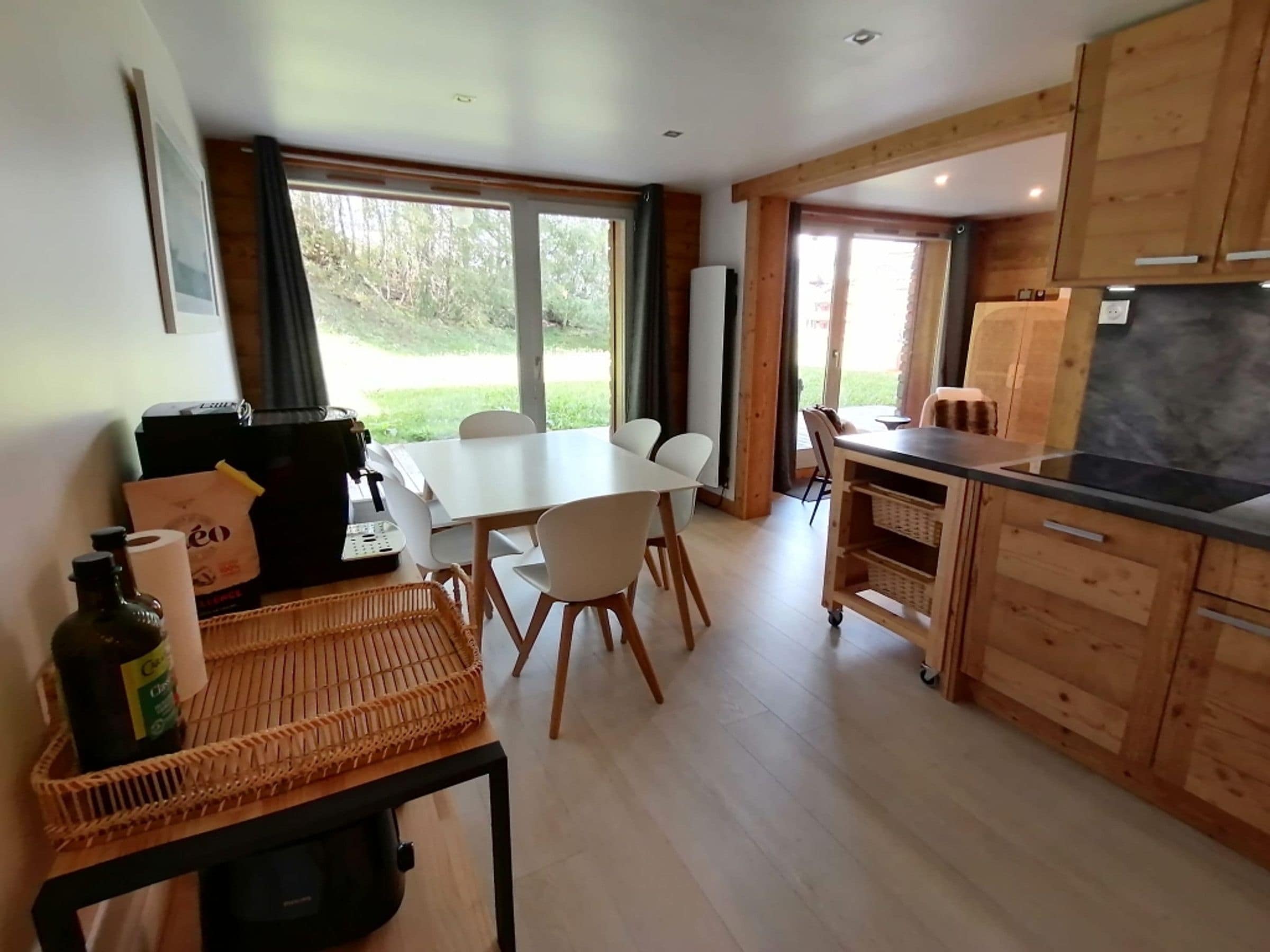 Een moderne keuken met houten kastjes, een eettafel met stoelen en een groot raam met uitzicht op groen.