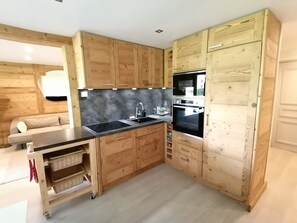 Cozinha compacta com armários de madeira, bancada preta e forno embutido.