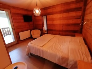 Ein Zimmer aus Holz mit einem Bett, einem Sessel, einem Fernseher und einer Tür zum Balkon.