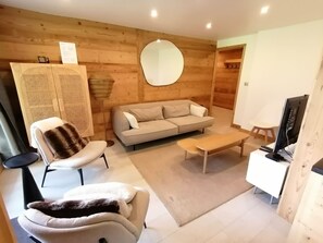Ein modernes Wohnzimmer mit einer Couch, einem Sessel, einem Couchtisch und einem Fernseher.