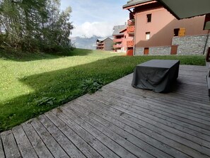 Eine Holzterrasse mit Tisch, einer Rasenfläche und einem Gebäude mit Balkonen.