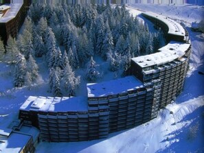A snow-covered building with a circular layout, surrounded by dense forest. - Charming apartment, balcony - 6 guests (Les Arcs 1800)
