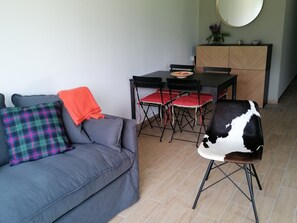 A living room with a grey sofa, a plaid pillow, a black and white chair, and a dining table with red cushions. - Luxury apartment near golf course - 4 guests (Barcelonnette)