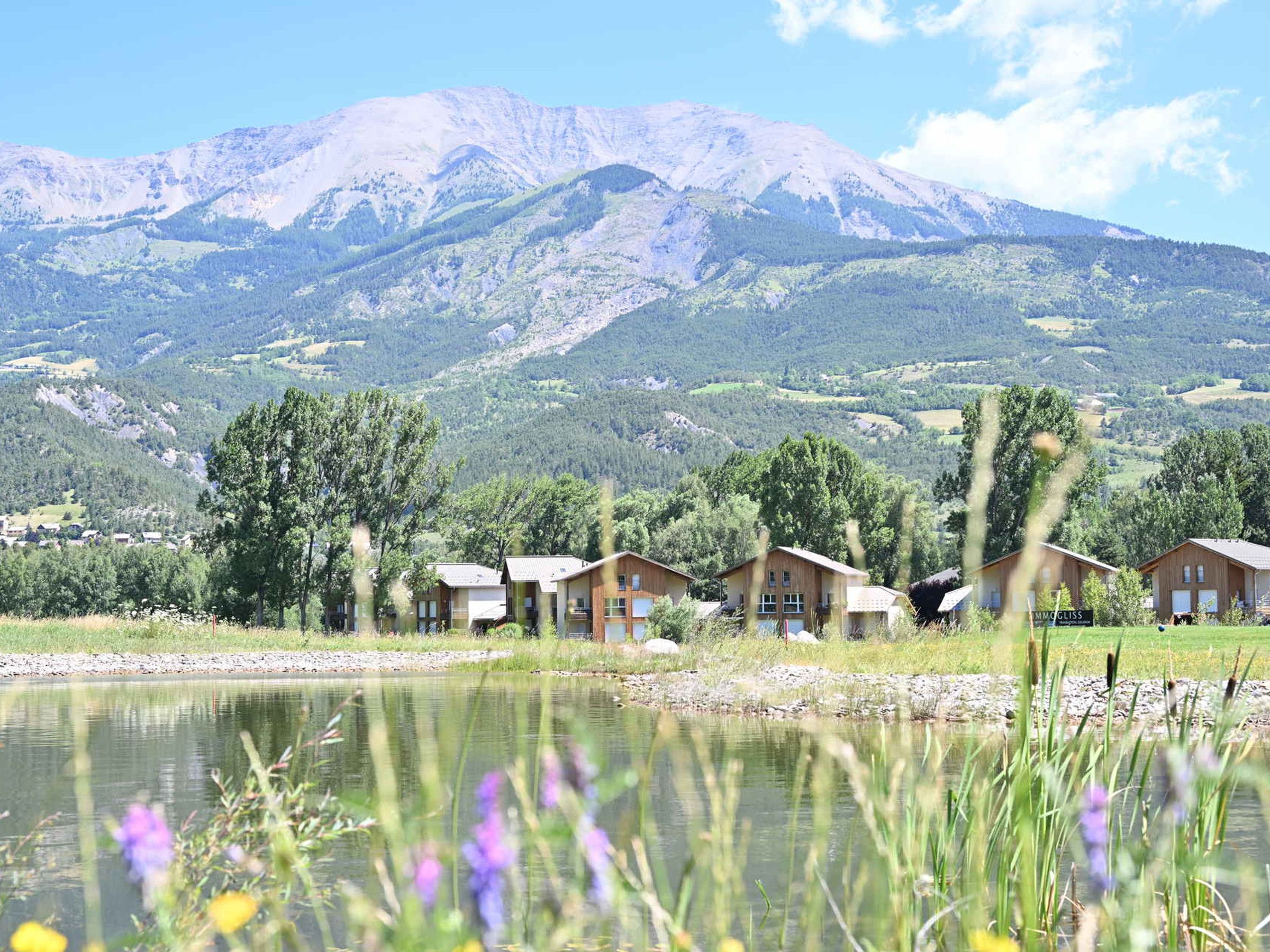 A lakeside view of a mountain range with wooden cabins.