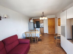 A compact living space with a red sofa, a dining table with chairs, a kitchen area with wooden cabinets, and a television on the right. - Apartment - 6 guests, mountain view (Orcières Merlette)