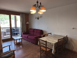 A room with a wooden dining table, a purple sofa, and a balcony with chairs. - Apartment - 6 guests, mountain view (Orcières Merlette)